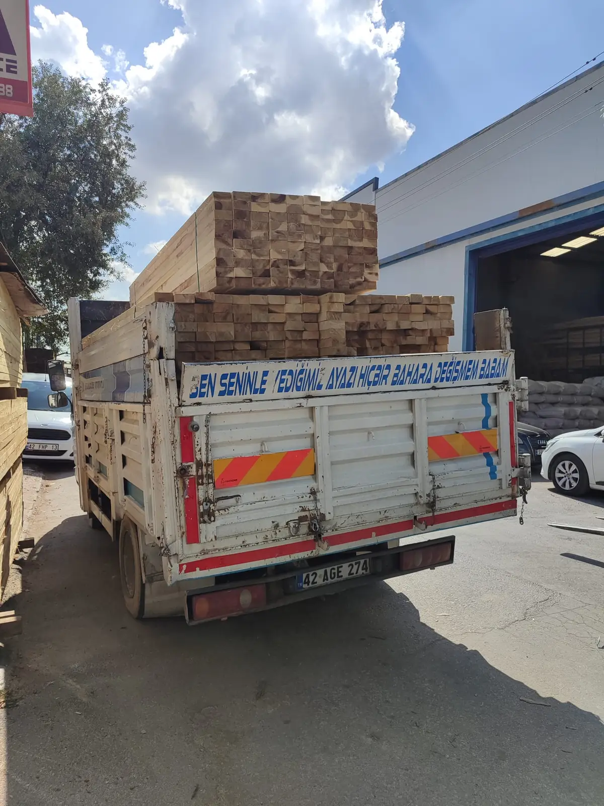 İki kat paketli kereste yüklenmiş kamyonet, depo önünde