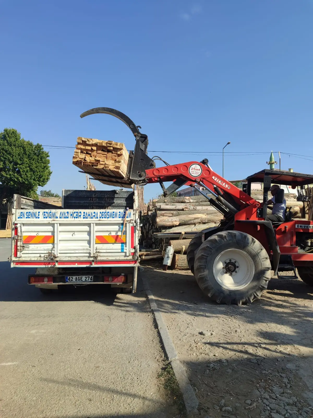 Kırmızı yükleyicinin paketli kereste bloğunu kamyonete koyması